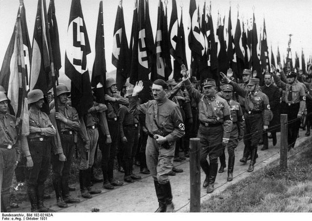 Adolf Hitler and Ernst Röhm walking through a formation of flags in Braunschweig